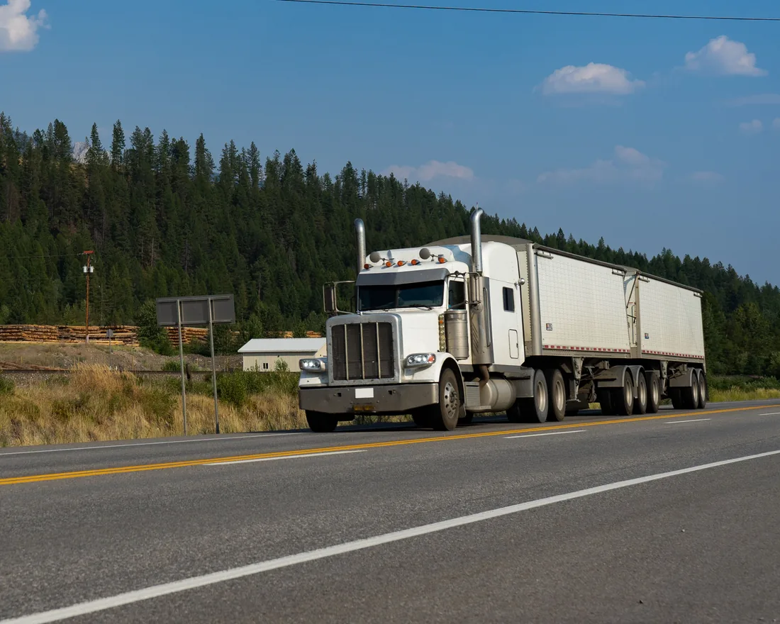 White tractor-trailer travelling along a forest-lined road in British Columbia